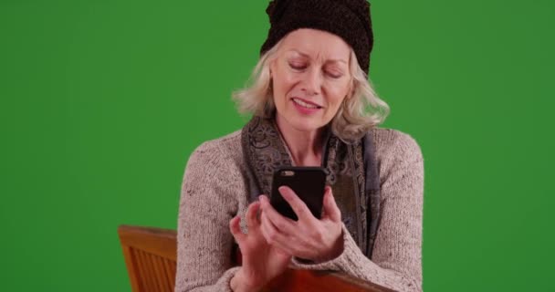 高齢の女性がベンチに座って携帯電話で緑の画面にメッセージを送る 陽気年上の女性テキストメッセージ上のスマートフォン緑の画面にキーイングまたは構成される — ストック動画