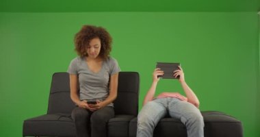 Çift yeşil ekranda kanepede oturan teknolojiyi kullanıyor. Anahtar ya da birleşik olmak üzere yeşil ekranda.