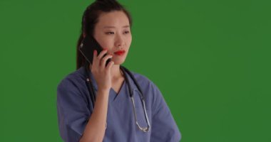 Genç Asyalı hemşire yeşil ekranda doktorla konuşmak için akıllı telefon kullanıyor. Güzel Asyalı hemşire yeşil ekranda cep telefonuyla konuşuyor. 4k