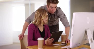 Başarılı erkek ve bayan meslektaşlar ofis içinde proje üzerinde birlikte çalışıyorlar. Erkek iş arkadaşı bilgisayarda yazarken iş kadını tablet kullanıyor. 4k