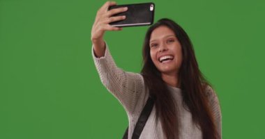 Güzel beyaz kadın yeşil ekranda akıllı telefonuyla selfie çekiyor. Mutlu genç bir kadın yeşil ekran duvarın önünde selfie çekmek için akıllı telefon kamerası kullanıyor. 4k