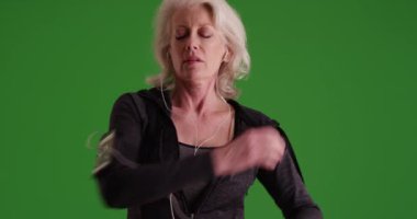 50 'li yaşlarının sonunda olgun bir kadın yeşil ekranda koşmak için kaslarını esnetiyor. Müzik dinleyen çekici yaşlı kadın yeşil ekranda koşmaya hazırlanıyor..