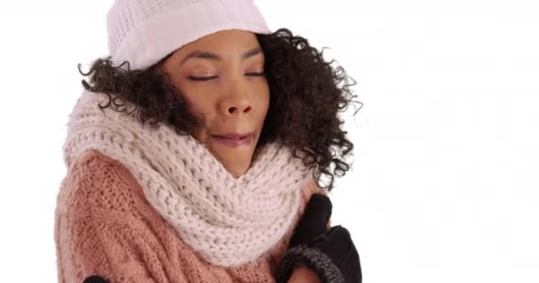 居心地の良い帽子とスカーフでかわいい黒い女性のクローズアップは 白い背景で暖めようとしています スタジオで震えて冬服を着たアフリカ系アメリカ人女性の笑顔のクローズアップ — ストック動画