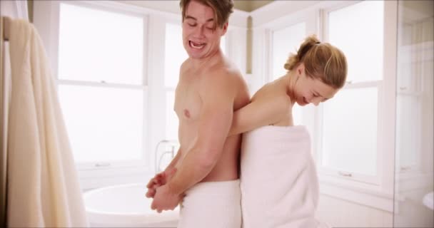 迷人的白种人夫妇背靠背站在浴室里 裹着毛巾 笑着笑着 女人们从相机上走下来 取出毛巾 扔向震惊的男朋友 — 图库视频影像