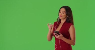 Kırmızı elbise giyen, cep telefonuyla müzik dinleyen ve yeşil ekranda dans eden tatlı Latin bir kadın. Anahtar ya da birleşik olmak üzere yeşil ekranda.