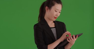 Asyalı neşeli iş kadını yeşil ekranda ayakta durmak için tablet kullanıyor. Genç profesyonel Çinli kadın yeşil ekranın önünde taşınabilir tablet bilgisayar üzerinde çalışıyor. 4k