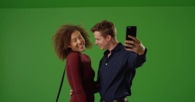 Mutlu melez çift yeşil ekranda selfie çekmek için akıllı telefon kullanıyor. Anahtar ya da birleşik olmak üzere yeşil ekranda.