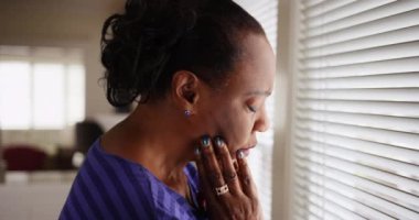 Yaşlı siyah bir kadın kederli bir şekilde pencereden dışarı bakıyor. Yaşlı bir Afrikalı Amerikalı kadın ne yazık ki penceresinden dışarı bakıyor. 4k