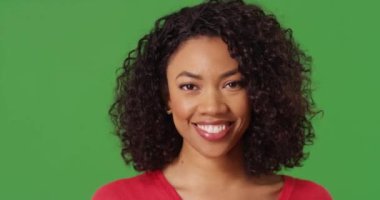 Güzel siyah bir kadının yeşil ekran arkaplanındaki kameraya bakıp gülüşünün yakın bir portresi. Mutlu Afro-Amerikan milenyumu yakın plan yeşil ekran üzerinde anahtarlama veya kompozitasyon için. 4k