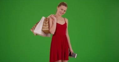 Yeşil ekranda omzunda alışveriş torbaları olan kırmızı elbiseli güzel, mutlu, beyaz bir kadın. Anahtar ya da birleşik olmak üzere yeşil ekranda.