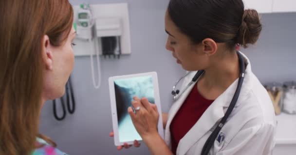 女性患者の首のX線をレビューするためにタブレットを使用して若い医師の肖像画 魅力的なラティーナ医師と高齢者のクローズアップ見ますX線の背骨と頭蓋骨 — ストック動画