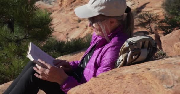 Szczęśliwa Starsza Pani Obozowiczka Siedząca Zewnątrz Piaskowcowym Kanionie Czytająca Książkę — Wideo stockowe