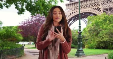 Paris Parkı 'nda akıllı telefon kullanan tatlı Latin kadın. Gülümseyen kadının portresi cep telefonunda adres tarifi uygulaması kullanıyor. 4k