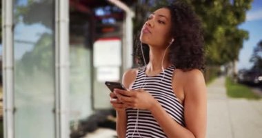Çizgili bluzlu şirin zenci kadın portresi cep telefonundan müzik dinliyor. Güzel Afrikalı kadın yaz günü açık havada şarkı söyleyerek dans ediyor. 4k