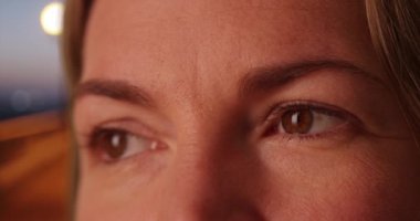 Geceleri iskelede beyaz bir kadının gözünün aşırı derecede kapanması. Orta yaşlı beyaz kadın okyanusa bakıyor, kahverengi gözlü. 4k