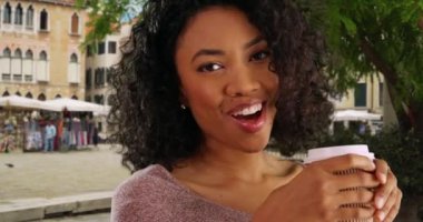 Venedik 'te fincandan kahve içen mutlu siyah kadın turist. İtalya 'da tatilde gülümseyen ve kahkahalar atan Afrika kökenli güzel bir Amerikalı kadını yakından çek. 4k