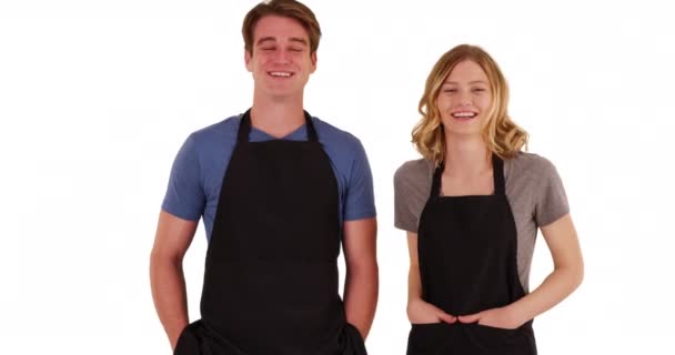 男男女女穿着围裙并排站在摄影棚里对着镜头笑的画像 两个厨师或伙食承办商 手插在围裙口袋里 白色背景 — 图库视频影像
