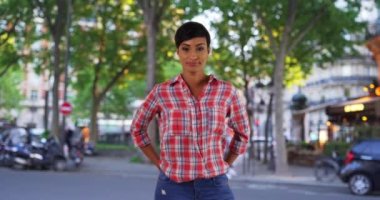 Şehirde gülümseyen Afrikalı Amerikalı kadın bahçıvanın sıradan portresi. Şehir sokağında dikilip doğrudan kameraya bakan çekici siyahi bir kadın. 4k