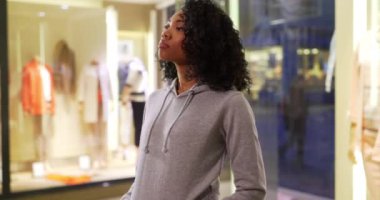 Gri kapüşonlu siyahi kadın gece vakti arkadaşını beklerken ileri geri sallanıyor. Güzel Afro-Amerikalı kız şehirdeki dükkana bakıyor. 4k