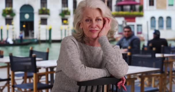 威尼斯运河边的咖啡馆庭院里坐着一位快乐的老年妇女 在意大利度假的老游客对着摄像机笑 — 图库视频影像