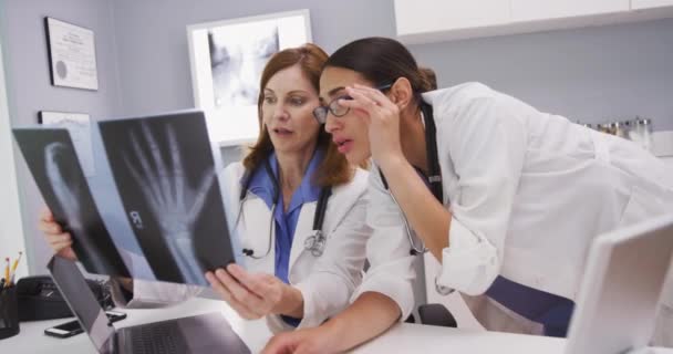 シニア同僚と手と手首の患者X線をレビュー美しい女性医師の肖像画 室内でMri検査を受ける2人の医師 — ストック動画