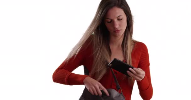 若い女性の固体白の背景にテキストを送信するために財布から電話を取る 白いコピースペースのテキストに返信するために袋からスマートフォンを引く若い女性 — ストック動画