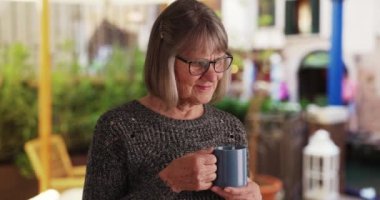 Bahçe bahçesinde elinde bir fincan kahveyle mutlu bir son sınıf kadını. Mutlu olgun bir kadın Venedik, İtalya 'da elinde içki tutarken mutlu görünüyor. 4k