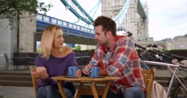 Tower Bridge 'de sohbet eden ve kahve içen çift. Beyaz bir erkek ve kadın Londra 'da sohbet ediyor ve kahvenin tadını çıkarıyor. 4k