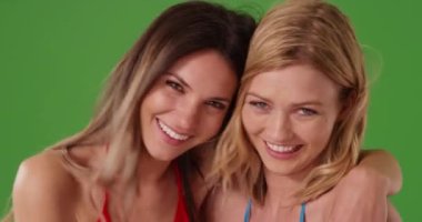 Mutlu genç kız arkadaşlar birlikte poz veriyorlar ve yeşil krom anahtar bileşimi için kameraya gülümsüyorlar. Kapalı alanda gülen sevimli kızların yakın çekimi. 4k