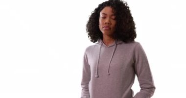 Gri eşofmanlı güzel Afro-Amerikalı kadın beyaz arka planda serin bir özgüvenle kameraya bakıyor. Stüdyoda muhteşem kıvırcık saçlı zenci kadın portresi. 4k