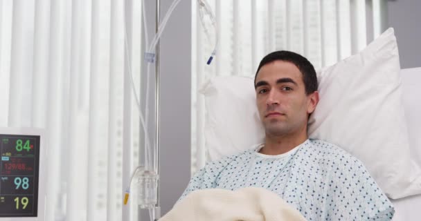 病院のベッドに横になってカメラを見ている大人の男性ラテン系患者の肖像画 手術を受けた後の回復における魅力的なパニック患者の近いビュー — ストック動画