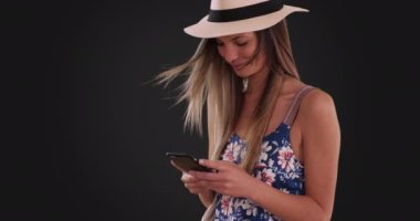 Çiçek desenli fötr şapkalı mutlu kadın gri arka planda telefonla mesajlaşıyor. Yirmili yaşlardaki bir kız, cep telefonundan gri arka planda mesaj atıyor. 4k