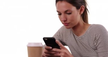 Milenyum kızı masada oturmuş beyaz arka planda akıllı telefondan mesaj atıyor. Beyaz fotokopi odasında kahve fincanı mesajlarıyla oturan genç beyaz bir bayan. 4k