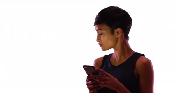 漂亮的非洲裔美国女性的肖像 她用智能手机用白色背景和彩色空间发短信 快乐的年轻女子一边打电话一边微笑着 一边在工作室里笑 — 图库视频影像