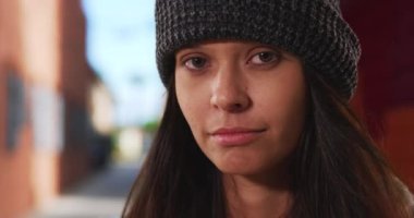 Bin yıllık bereli bir kızın şehir sokağının önündeki kameraya bakışının yakın portresi. Şehir merkezinde rüzgar gibi esen saçları olan 20 'li yaşlarda beyaz bir kız. 4k