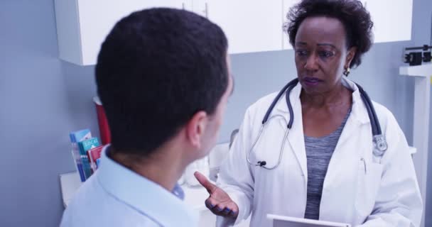 近距离观察黑人医生与年轻男性病人讨论健康问题 非洲资深医生使用便携式平板电脑记录病人的健康状况 — 图库视频影像