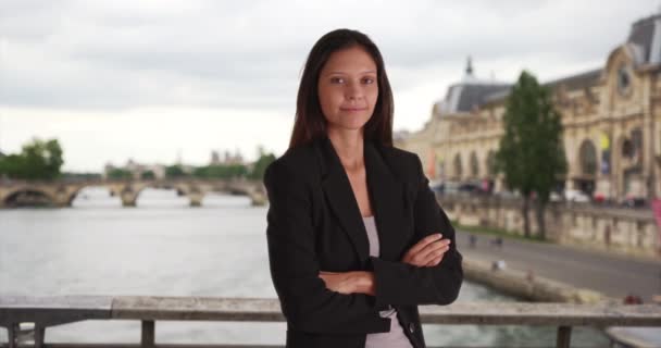 パリの橋の上で若いビジネスマンの女性がカメラで笑っているのを自信を持って フランスでの出張中にレンズを見ているビジネスマン — ストック動画