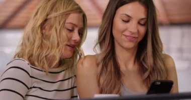 Sarışın, esmer bir kadının evde akıllı telefon göstermesine yakın çekim. Evin içinde akıllı telefonu paylaşan iki arkadaşın yakın görüntüsü. 4k