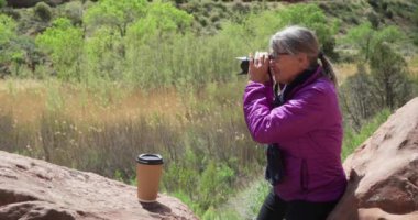 Kanyonda dinlenirken doğanın fotoğraflarını çeken eski bir doğa meraklısı. Olgun doğa aşığı kadın Zion Utah 'taki vahşi hayatın fotoğraflarını çekmek için kamera kullanıyor.
