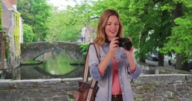 Bruges 'deki seyahat fotoğrafçısı dışarıda gülümserken fotoğraf çekiyor. Kamerayla fotoğraf çeken mutlu kadın turist. 4k