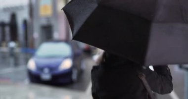 Aptal yaşlı kadın siyah şemsiyeyle yağmurun altında dans edip zıplıyor. Neşeli yaşlı kadın yağmurlu bir günde dışarıda eğleniyor ıslak kaldırımda şemsiyeyle dönüyor. 4k