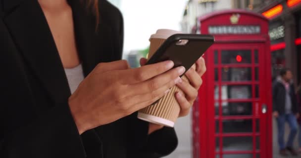ロンドンのダウンタウンにいる間 スマートフォンで女性の手のテキストメッセージを閉じます 英国への出張中に路上で携帯電話を使用して女性のタイトなショット — ストック動画