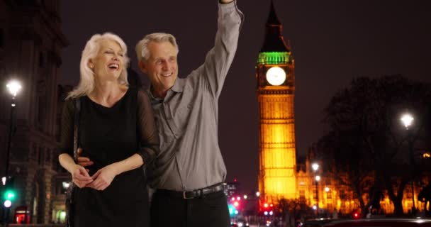 笑着的一对成熟的夫妇在伦敦的夜晚欢呼出租车 迷人的白人男性和女性叫出租车的肖像 — 图库视频影像