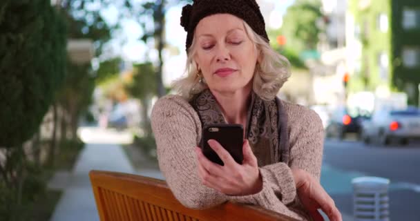 Starsza Kobieta Siedząca Ławce Przy Ruchliwej Ulicy Patrząca Telefon Atrakcyjna — Wideo stockowe