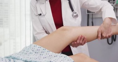 Genç kadınlara bakan tıp doktoru klinikte dizinden yaralanmış. Hastanenin içinde yaralı bacağı olan genç bir kadın hasta yatarken kıdemli doktor onu tedavi ediyor.