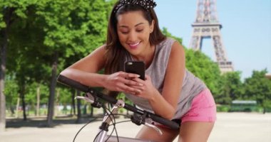 Bisikletli, cep telefonundan mesaj atan çekici bir Latin kadın. Paris 'te gülümseyen genç bir kadın 4G cihazı kullanıyor. 4k