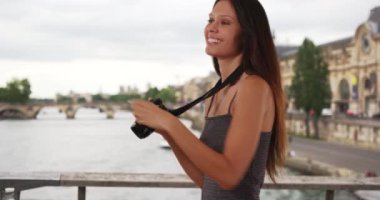 Güzel gezgin fotoğrafçı Seine nehrinin üzerinde kamerayla fotoğraf çekiyor. Paris, Fransa 'da fotoğraf çeken mutlu genç bir kadının portresi. 4k