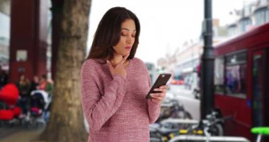 Güzel Latin kadın Londra caddesinde akıllı telefonunu kullanıyor. Dışarıda 4G cihazı kullanan genç bir kadının portresi. 4k