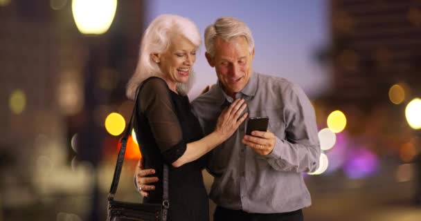 一緒にスマートフォンを使って夜のうちに幸せな高齢者 高齢者のカップルは 市内で夜と携帯電話を使用しています — ストック動画