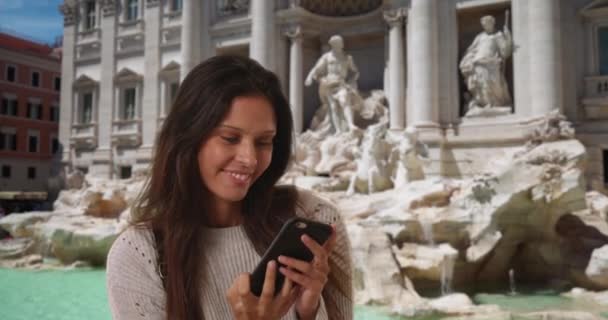 灰色のセーターを着た100万人の女性がトレビの泉の前で電話自慰行為をする ローマの女性バックパッカー観光客や友人と共有する携帯電話で写真を撮る — ストック動画